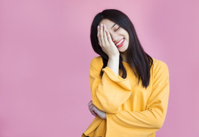 woman in a colorful top and background covering her face while smiling