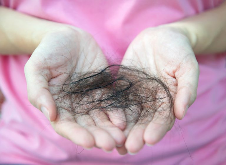 Close-up of woman hand in pink t-shirt hold loss hair, after taking shower, concepts of loosing hair or breast cancer.