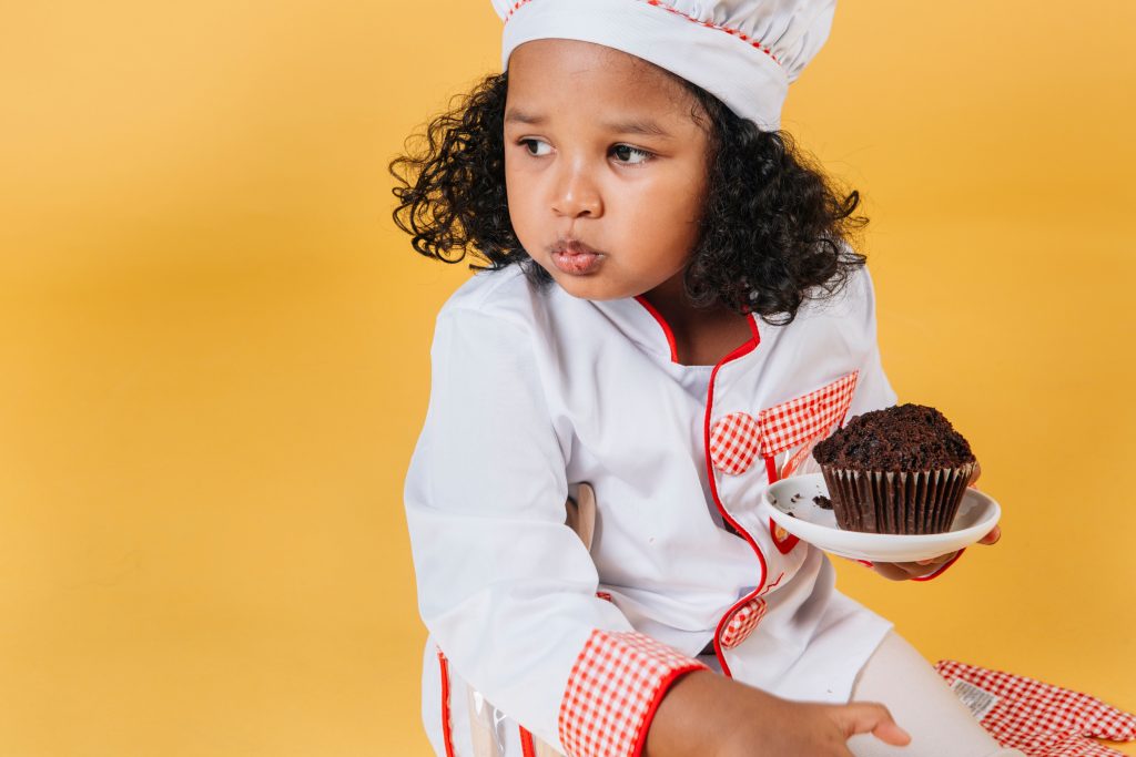 girl dressed as a chef holding a plate with a cupcake
