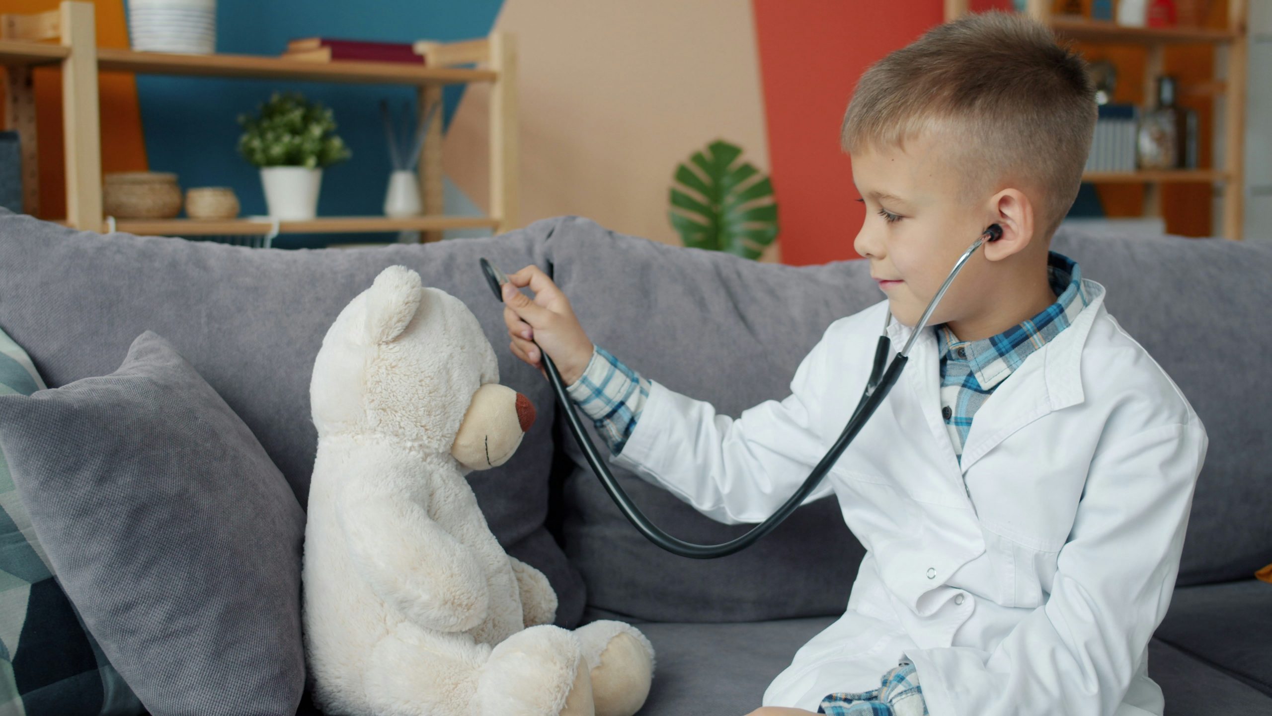 boy dressed as a doctor, pretending to examine a white teddy bear using a toy stethoscope